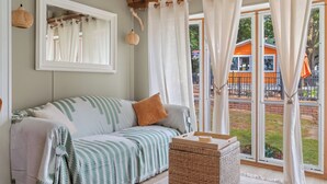 Ein Zimmer mit einer Couch, einem Korbwannenmöbel und Blick auf einen Außenbereich mit Zaun und einem Gebäude.