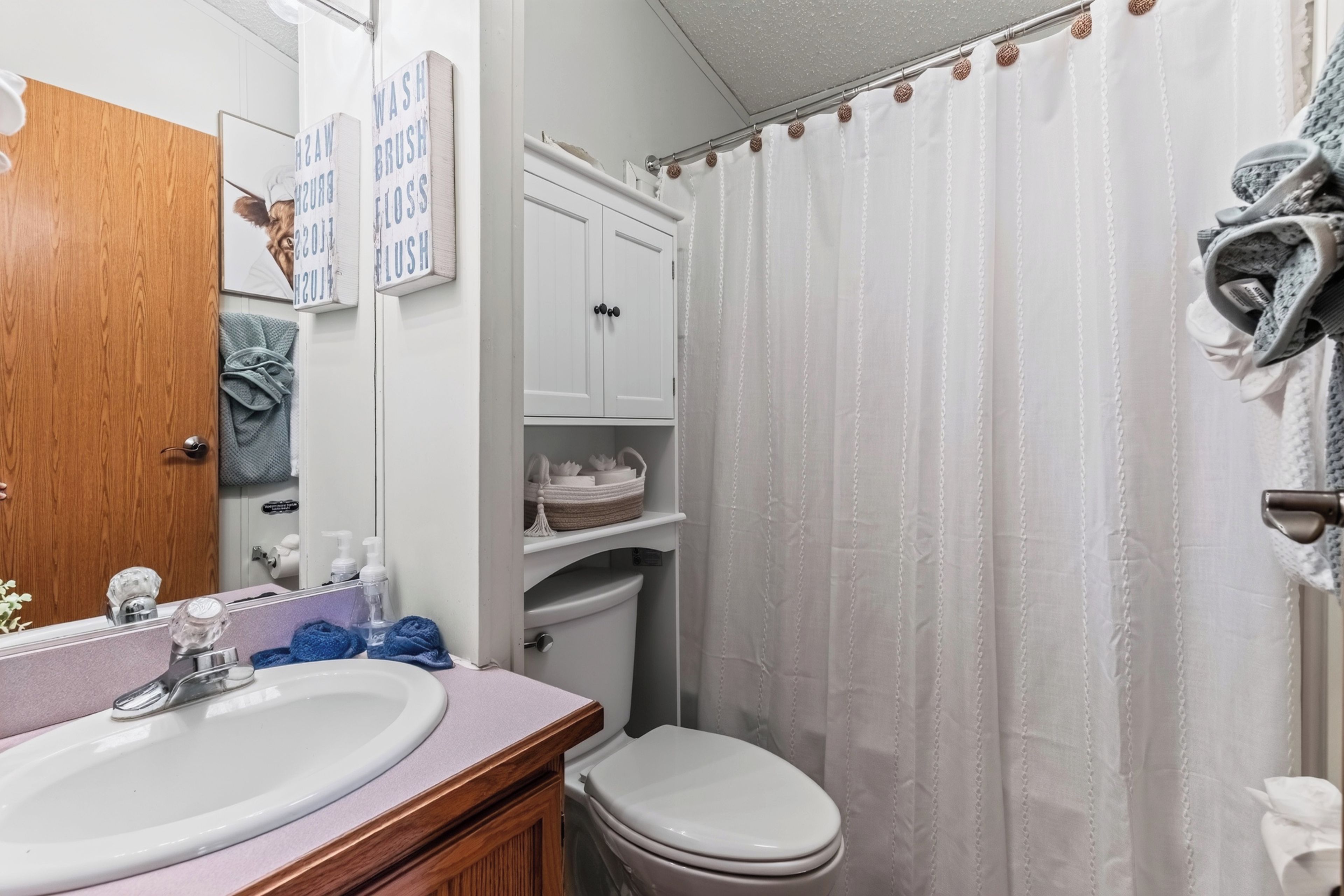 Un baño con lavamanos, espejo, armario, inodoro y cortina de ducha.