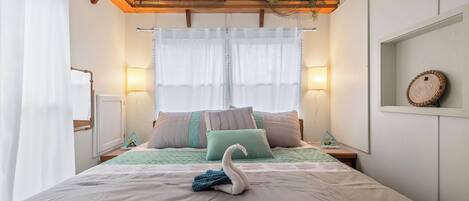 A bedroom with a bed, pillows, a swan decoration, a wall-mounted lamp, and a shelf with a decorative item.