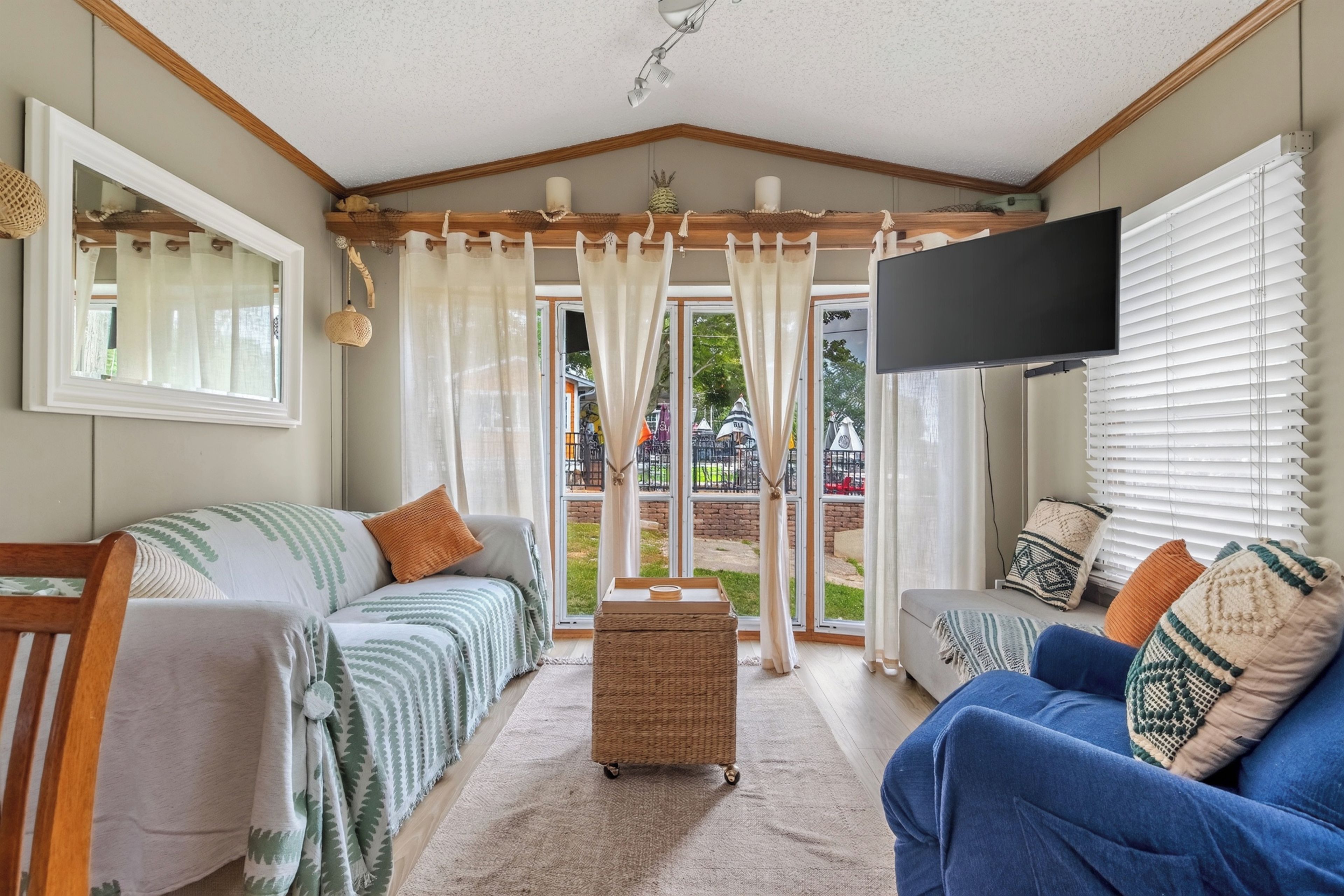 A cozy living room with a sofa, a television, and a large window with curtains.