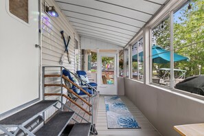 A covered outdoor area with a set of stairs leading to a door, a small table, and a view of the outside.