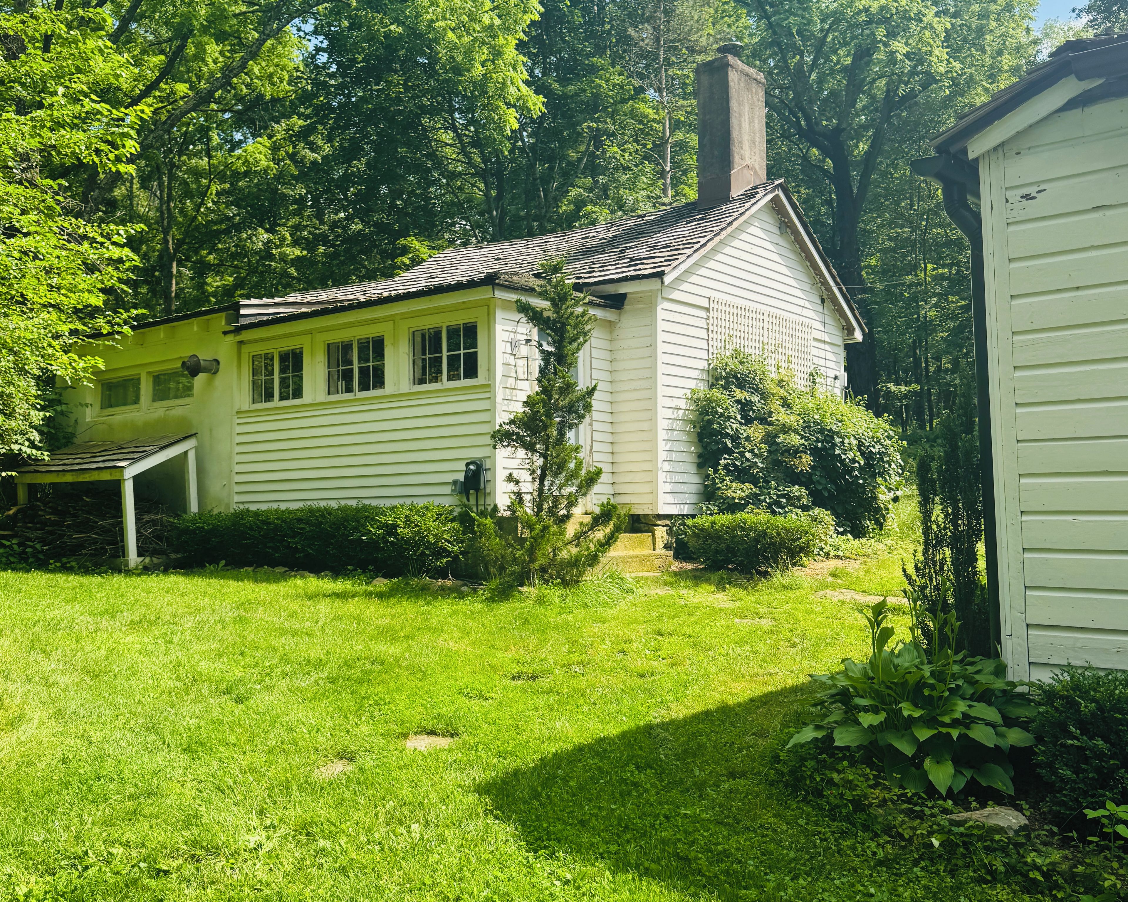 A single-story house with a gabled roof, surrounded by a well-maintained lawn and dense trees.