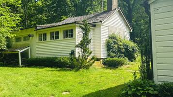 A single-story house with a gabled roof, surrounded by a well-maintained lawn and dense trees.