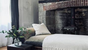 Quarto acolhedor com lareira de pedra, um sofá, uma mesa pequena com um vaso e um tapete.