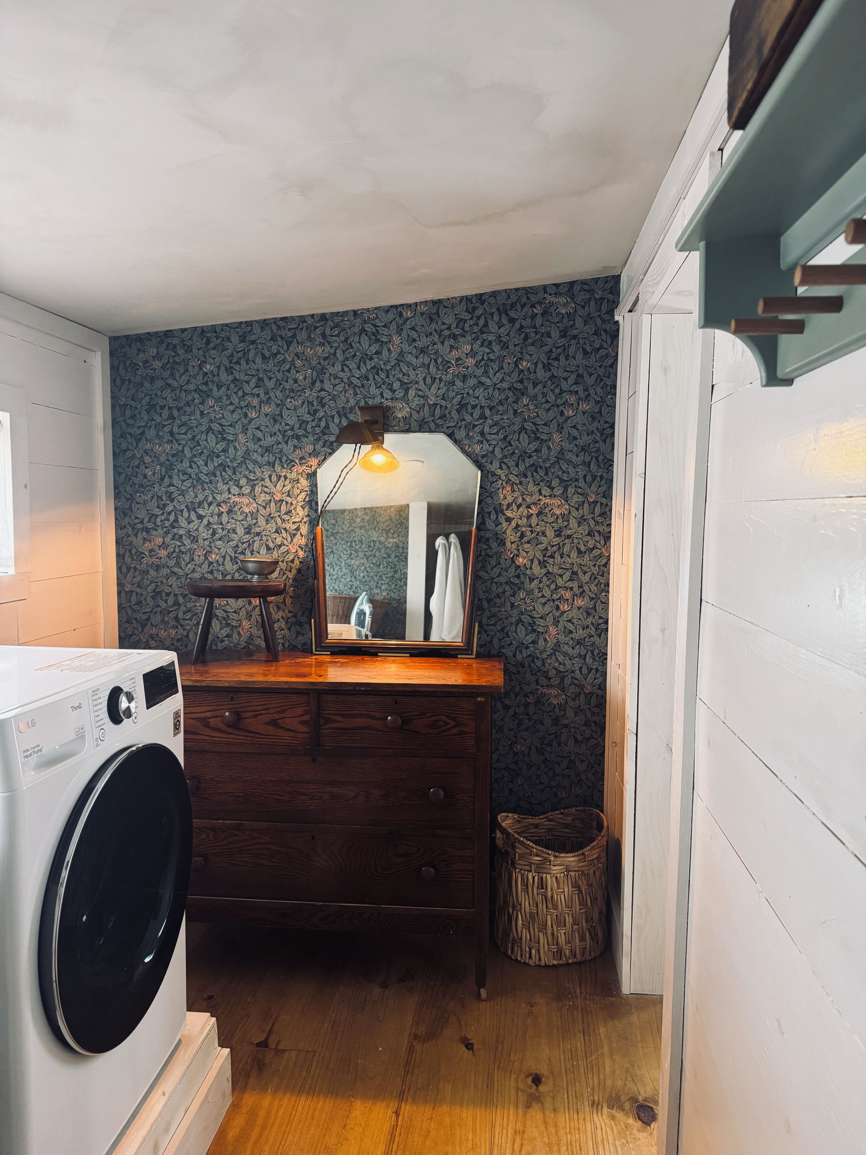 A laundry area with a washing machine, a wooden dresser, a mirror, and a wicker basket.