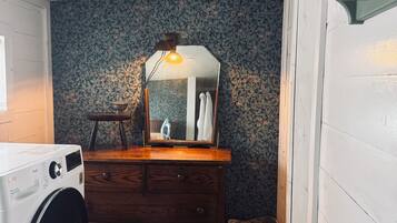 A laundry area with a washing machine, a wooden dresser, a mirror, and a wicker basket.