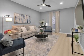 A modern living room with a sofa, coffee table, and chairs, a ceiling fan, and a large abstract painting. - Julie: 1 Bedroom Apt, 4 minute walk to A&M (College Station)