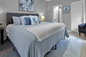 Een slaapkamer met een groot bed, een nachtkastje, een lamp en een deur.