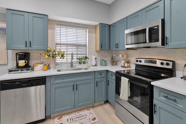 A modern kitchen with blue cabinets, stainless steel appliances, and a window with blinds.
