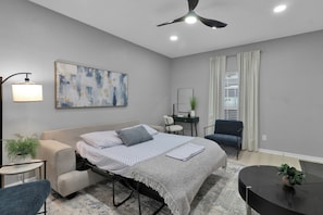 A modern bedroom with a bed, bedside tables, a desk, and a ceiling fan.