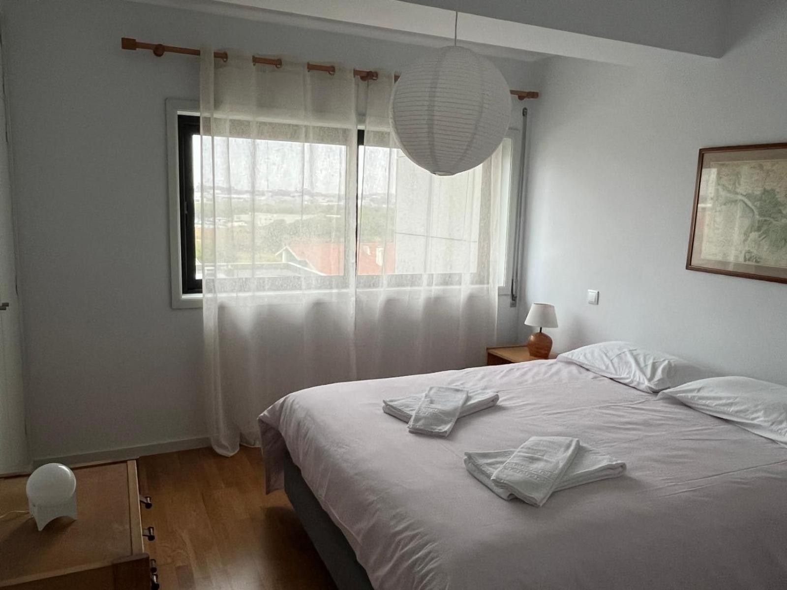 Quarto com cama, janela com cortinas, luminária de cabeceira e luminária na parede.