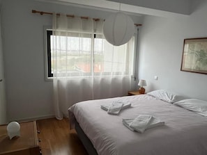 A bedroom with a bed, a window with curtains, a bedside lamp, and a wall-mounted light fixture. - Apartment 'Praia Azul' with Sea View, Balcony and Wi-Fi (Vila do Conde)