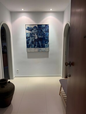 Un couloir avec une grande peinture abstraite au mur, une porte sur la droite et un objet sombre sur le sol.