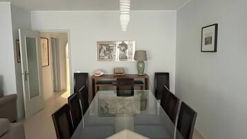 Uma sala de jantar com uma mesa de vidro cercada por cadeiras, um lustre e quadros na parede.