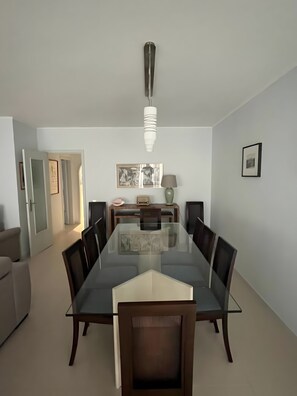 Une salle à manger avec une table en verre entourée de chaises, un luminaire suspendu et des œuvres d’art encadrées accrochées au mur.