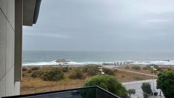 Vista de um parque de estacionamento com carros, uma praia e uma linha costeira rochosa.