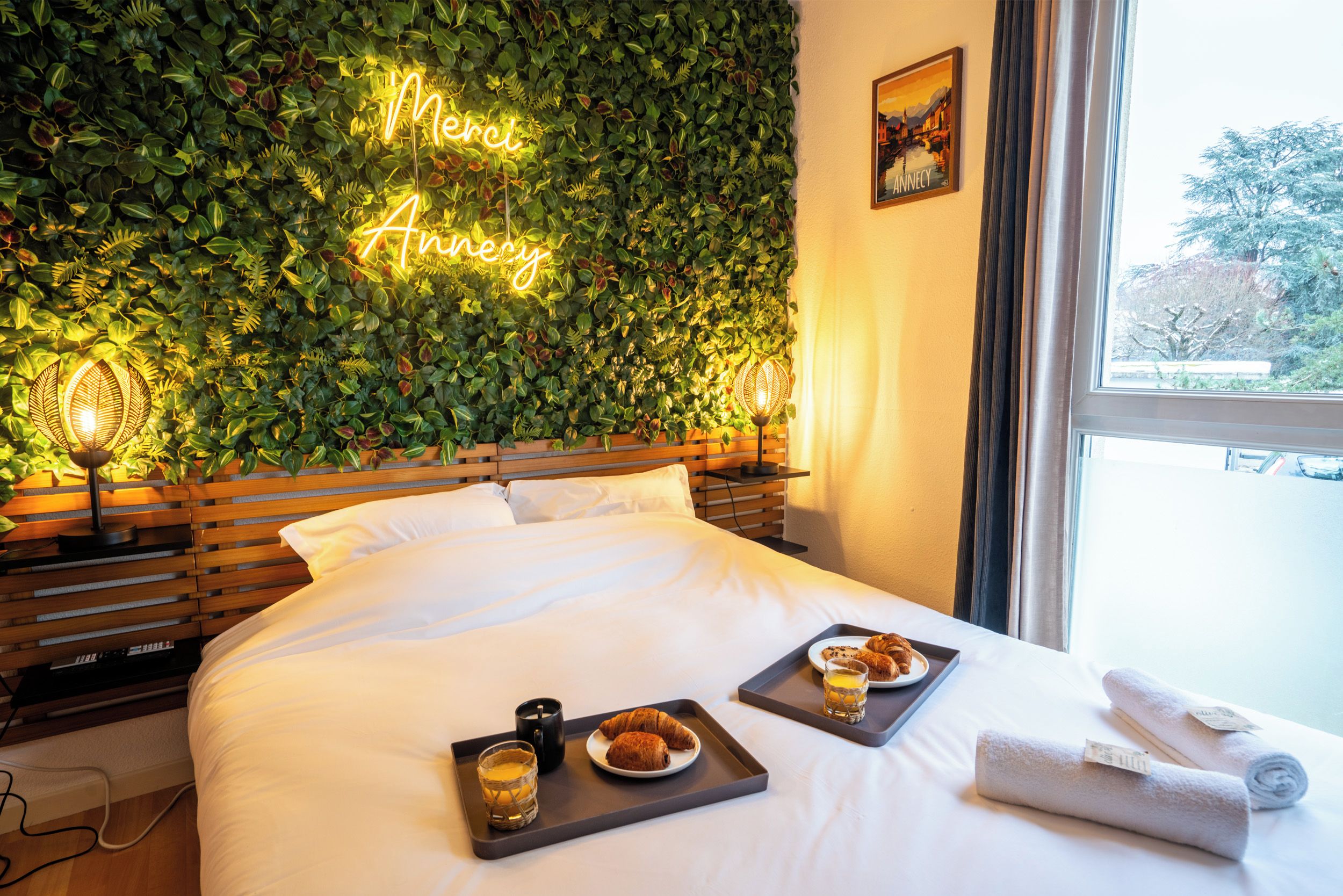 Une chambre d’hôtel avec un lit, un néon accroché au mur et des plateaux de petit-déjeuner posés sur le lit.
