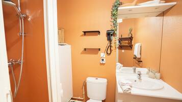 A bathroom with a white toilet, a sink, and a shower. There are shelves and a mirror above the sink.