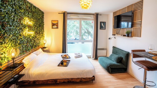 Une chambre d’hôtel avec un lit, un canapé vert, un coin repas et un téléviseur fixé au mur.