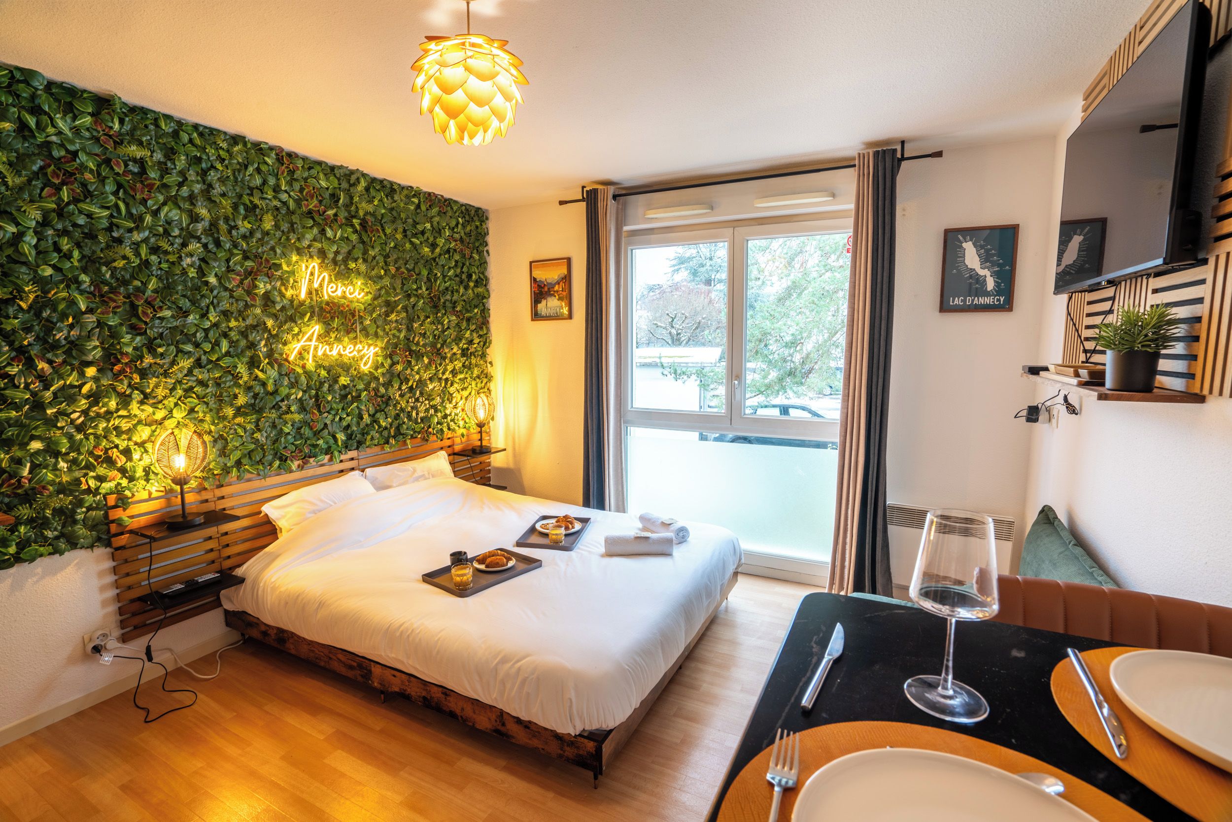 A hotel room with a bed, bedside table, and a view of the outside.