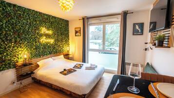A hotel room with a bed, bedside table, and a view of the outside.