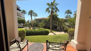 A balcony with a table and chairs, overlooking a well-maintained garden with palm trees and a hedge. - Vrbo Property (Cabo San Lucas, BCS)