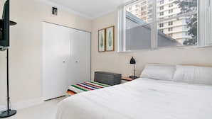 A bedroom with a bed, a wardrobe, a desk with a lamp, and a window with a view of buildings. - The Tides Hollywood Luxury Suites (Hollywood)