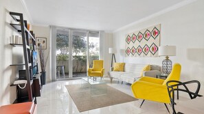 Un saló modern amb un sofà, butaques grogues, una taula de centre de vidre i una finestra gran.