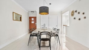 Comedor con una mesa rectangular, seis sillas, una lámpara colgante, un espejo enmarcado y una puerta con letrero de privacidad.