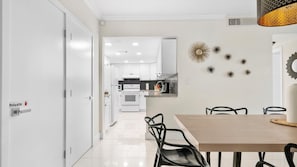 A modern kitchen with white cabinets, a dining area with a wooden table and black chairs, and decorative wall art. - The Tides Hollywood Luxury Suites (Hollywood)