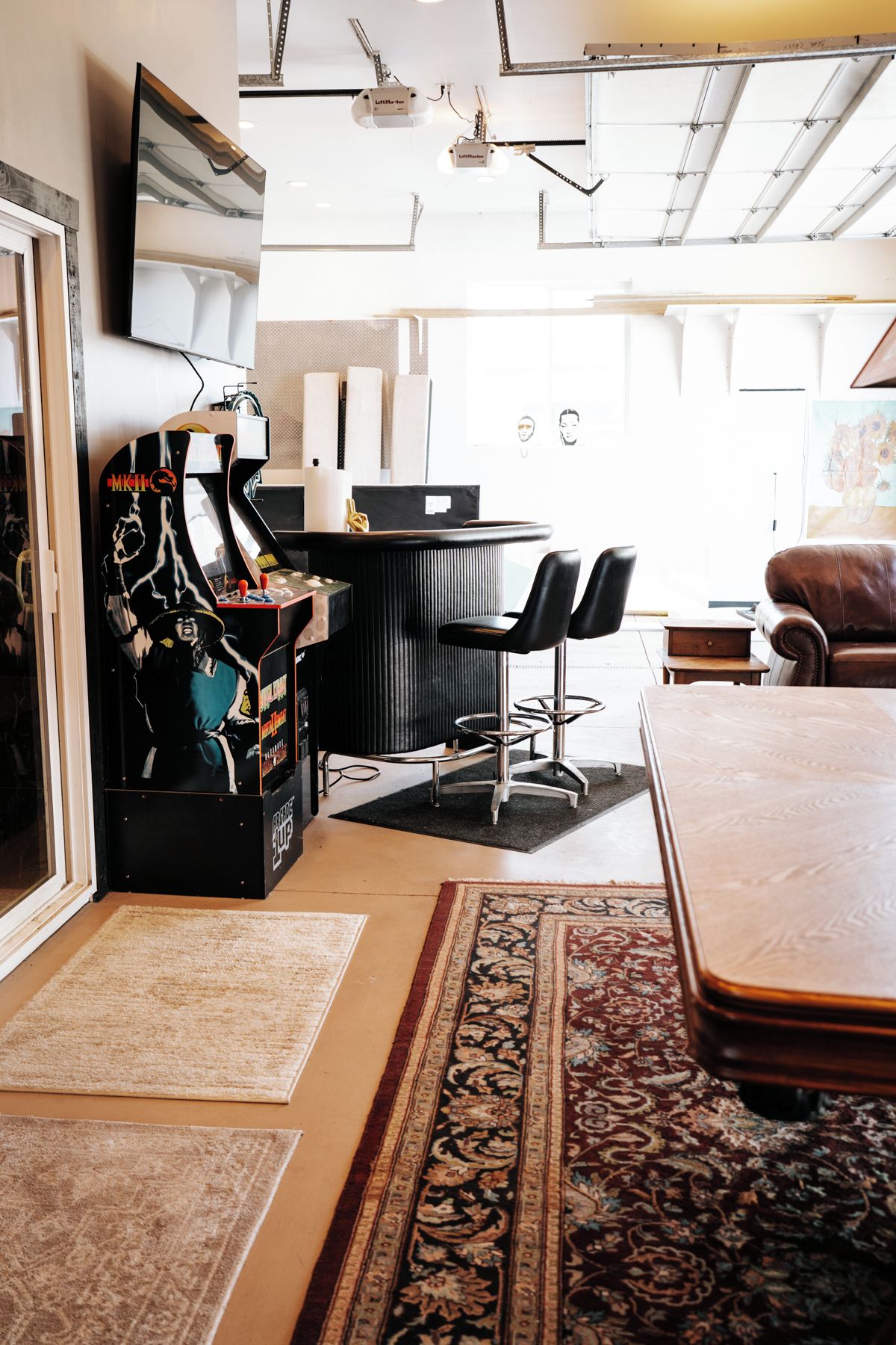 A modern living room with a large coffee table, a black leather sofa, a patterned rug, and a gaming console.