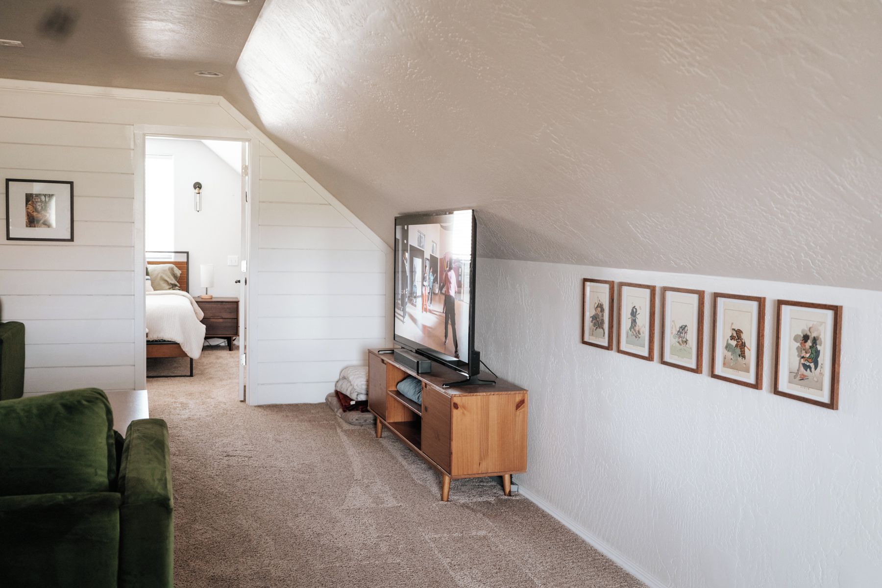 A room with a television on a wooden stand, a green sofa, and a bed with a white headboard.