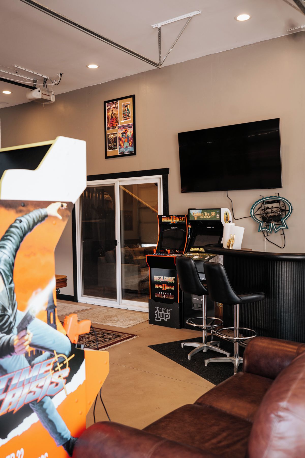 A living room with a large flat-screen TV, arcade games, a couch, and a glass door leading to another room.