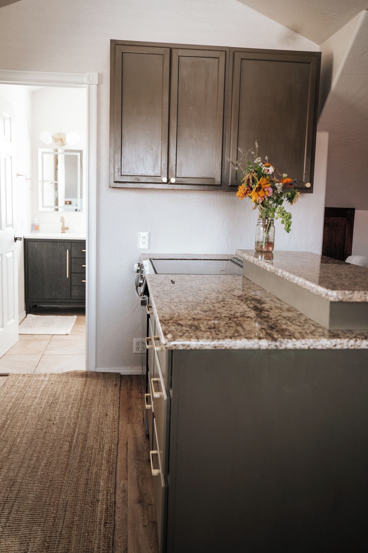 Une cuisine avec des meubles de couleur sombre, un plan de travail en granit et un plancher en bois.