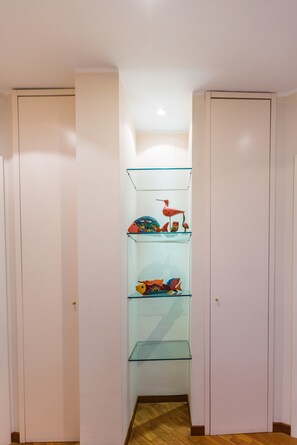 A narrow hallway with a glass shelf unit containing decorative items.