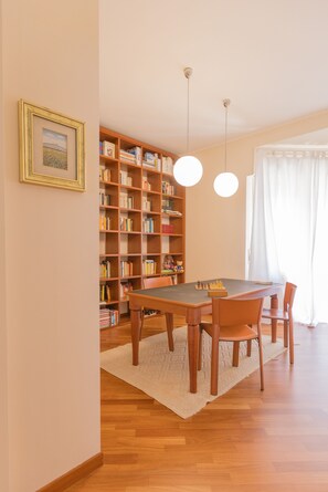 A dining area with a wooden table, chairs, a chessboard, and a bookshelf filled with books.
