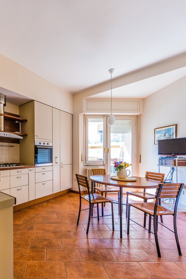 A kitchen with a dining area, a TV, and a window with blinds.