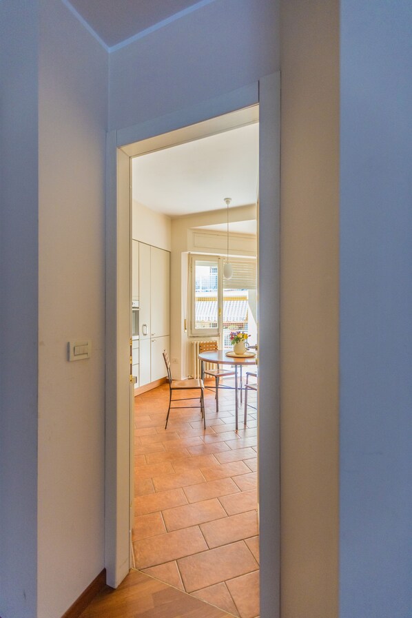 A hallway leading to a dining area with a table and chairs, a window with blinds, and a radiator.