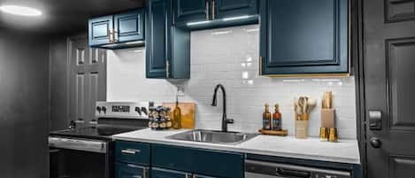 A modern kitchen with dark cabinetry, stainless steel appliances, and a light wood floor.