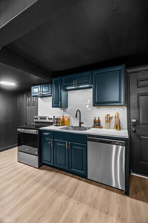 A modern kitchen with dark cabinetry, stainless steel appliances, and a light wood floor. - Bungalow 15 min to Downtown & Cherokee St (St. Louis)