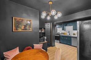 A modern kitchen with dark cabinetry, a wooden dining table, and a chandelier. - Bungalow 15 min to Downtown & Cherokee St (St. Louis)