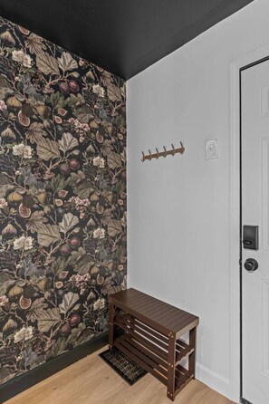 Een kamer met donker bloemenbehang, een houten bankje, een witte deur en een kapstok.