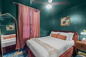 Ein Schlafzimmer mit einem Bett, einem Nachttisch, einem Spiegel, einem Deckenventilator und einem Gemälde an der Wand.