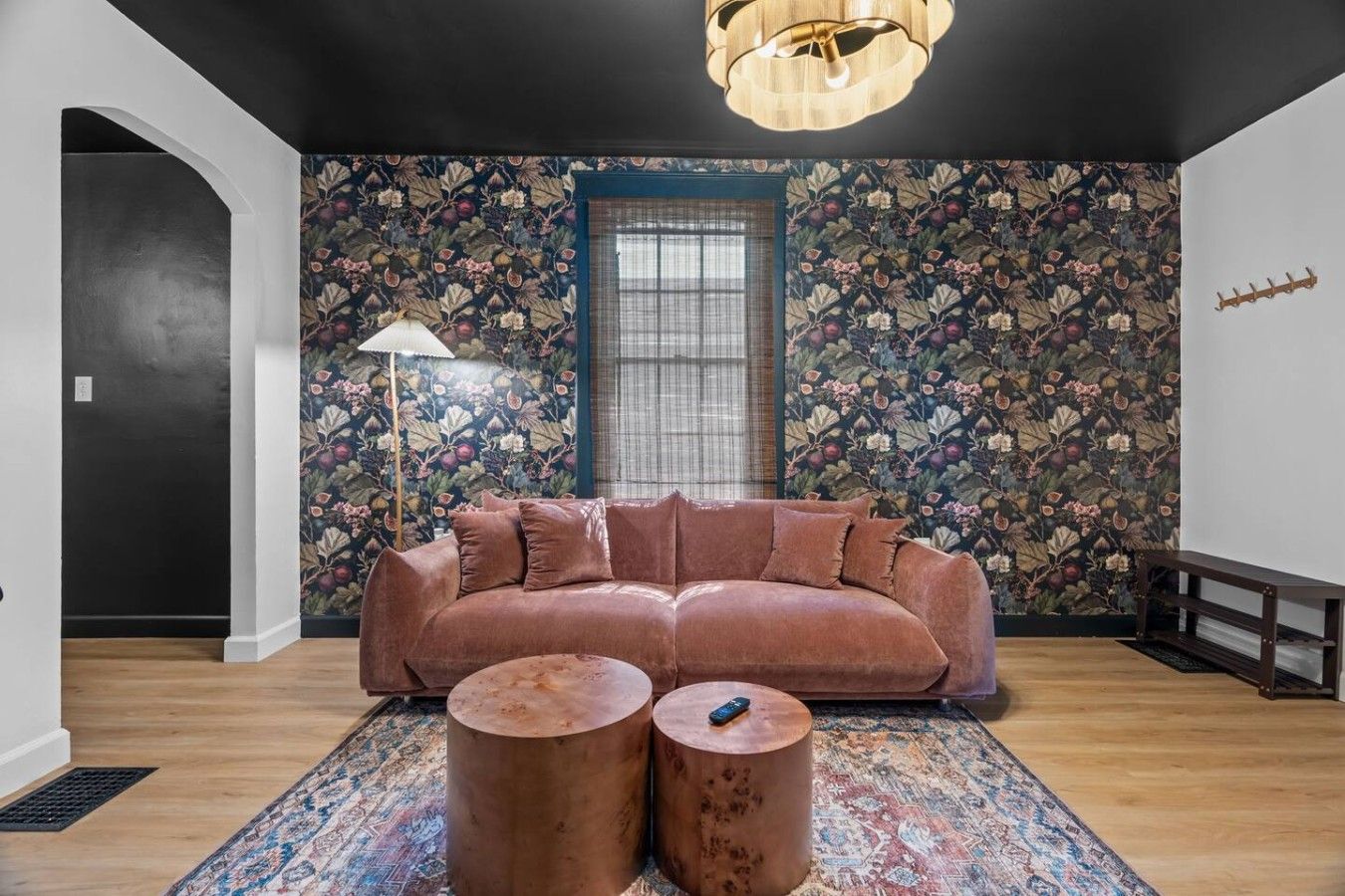 Een kamer met een ruime bank, twee ronde salontafels, een kamerkleed met dessin en bloemenbehang.