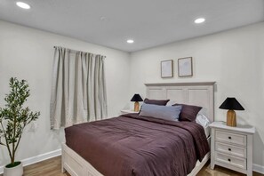 A bedroom with a bed, two bedside tables, a potted plant, and a window with curtains. - Heated Pool - Waterfront - 14 acre - 7bd 6ba (Friendsville)
