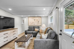 A living room with a flat-screen TV, a gray sofa, a wooden coffee table, and a patterned rug. - Heated Pool - Waterfront - 14 acre - 7bd 6ba (Friendsville)