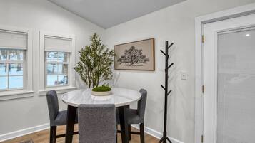 A dining area with a round table, four chairs, a potted plant, a coat rack, and a framed picture on the wall.