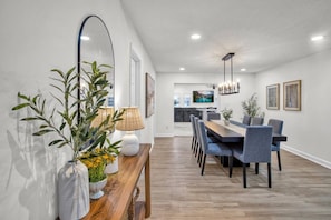A modern dining area with a wooden table and chairs, a mirror, and a lamp.