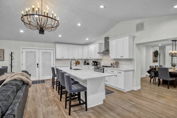 A modern kitchen with white cabinetry, a central island with bar stools, and a chandelier.