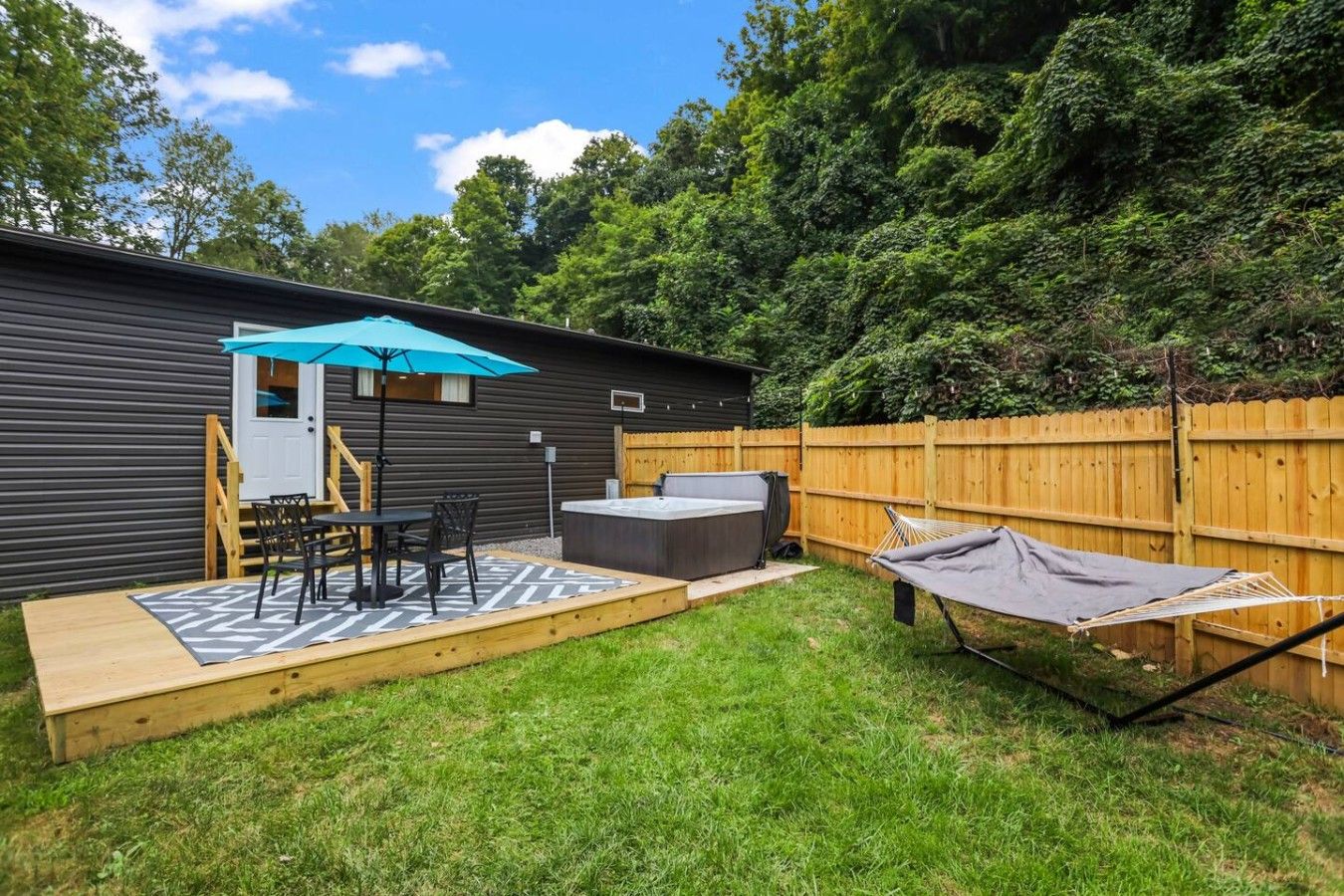 Ein Garten mit Whirlpool, Hängematte und einer Terrasse, komplett mit Tisch und Stühlen.